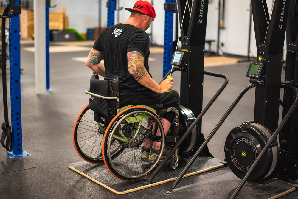 Pictured Chris "Stouty" Stoutenberg up close on a Concept2 Rower using the Equip Products Wider Ski Erg Base, in a gym setting on a black floor.