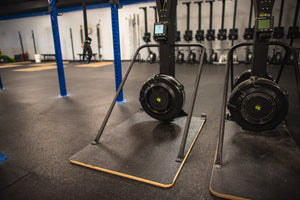 
            
                Load image into Gallery viewer, Pictured are two Concept2 Ski Erg&amp;#39;s, one with an Adaptive Base By Equip Products, and the other a standard size 24&amp;quot; base in a gym setting on a black floor.
            
        