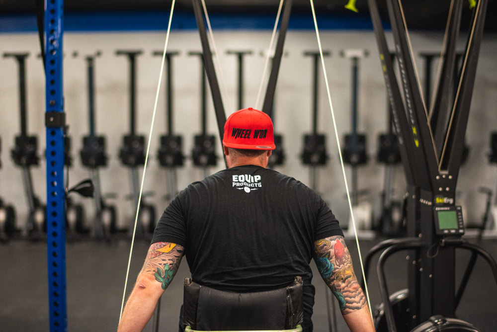 Close up shot of Chris "Stouty" Stoutenberg from the back using a Concept2 Ski Erg with the Equip Products Wider Adaptive Base for wheelchair athletes.