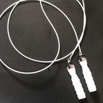 A White jump rope and handles by Rx Smart Gear made exclusively for Equip Products. Used for visually impaired athletes, the jump rope is sitting on a black gym floor.